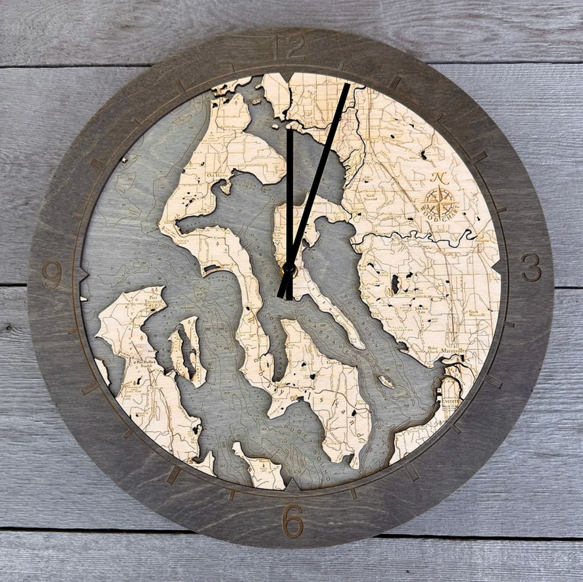 Whidbey & Camano Islands, Washington wood ring clock in laser-cut Baltic birch, shown against a weathered grey wall
