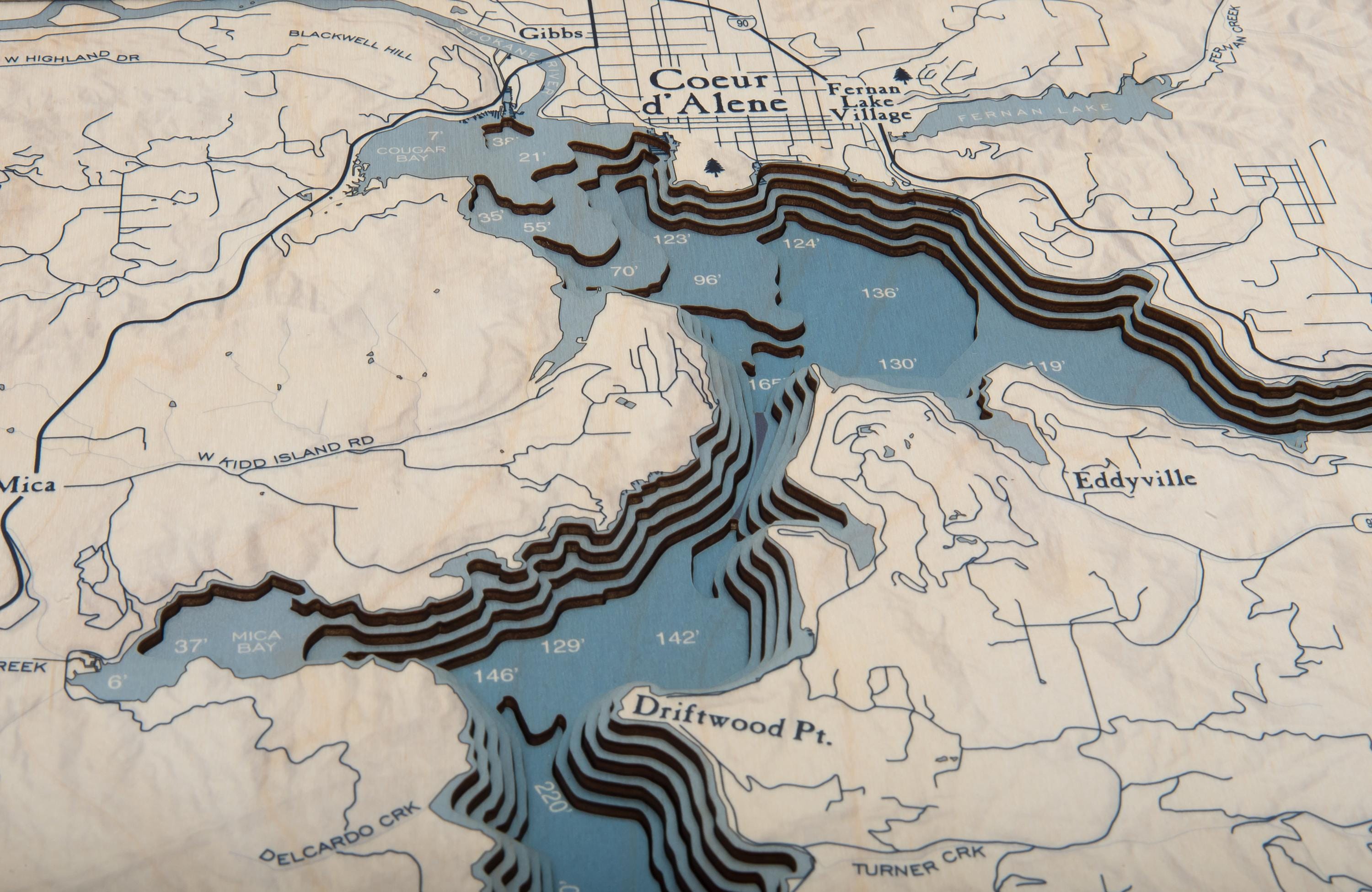 Lake Coeur d'Alene, Idaho 3D layered wood map in laser-cut Baltic birch, shown framed against a light wall