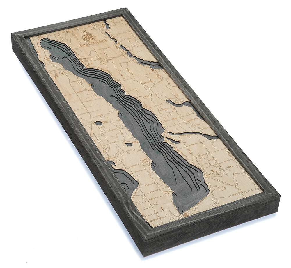 Torch Lake, Michigan 3D layered wood map in laser-cut Baltic birch, shown framed against a light wall
