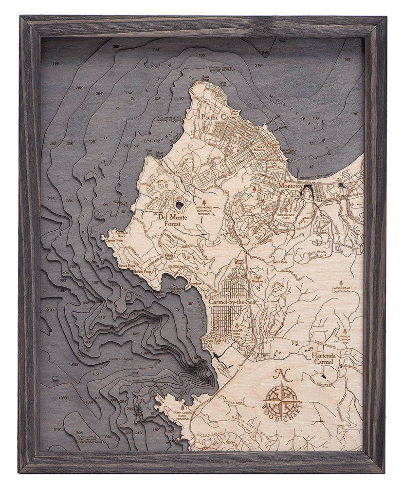 Carmel & Monterey, California 3D layered wood map in laser-cut Baltic birch, shown framed against a light wall