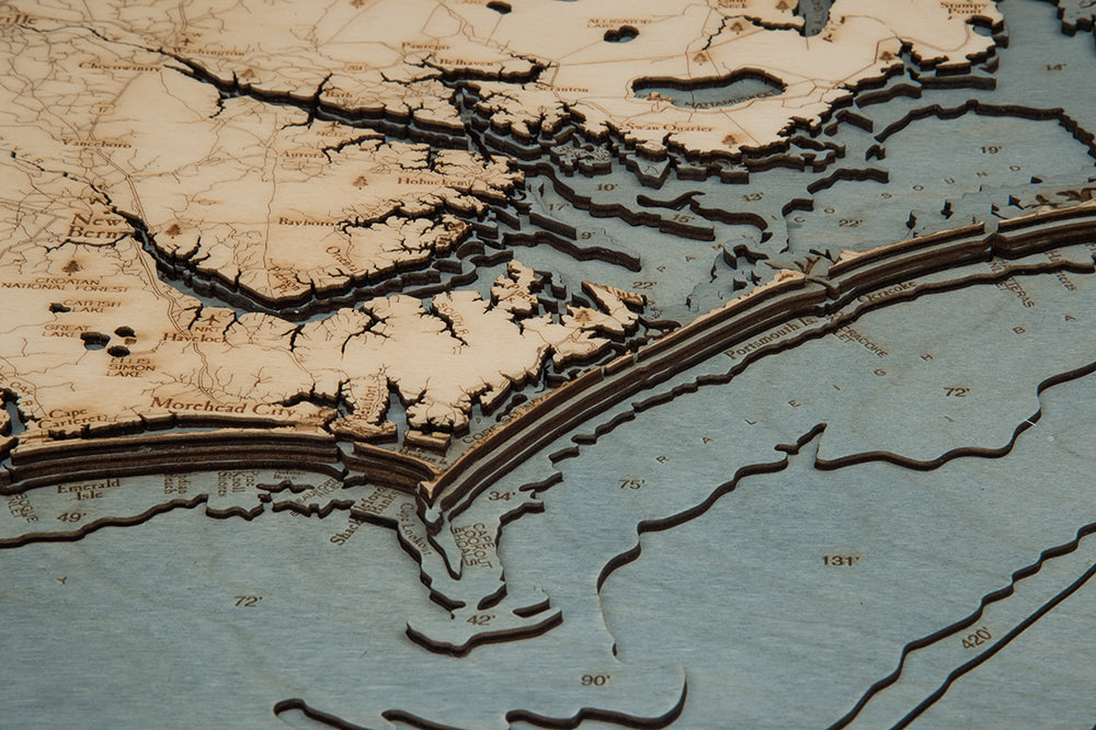 North Carolina Coast 3D layered wood map in laser-cut Baltic birch, shown framed against a light wall