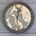 Whidbey & Camano Islands, Washington wood ring clock in laser-cut Baltic birch, shown against a weathered grey wall
