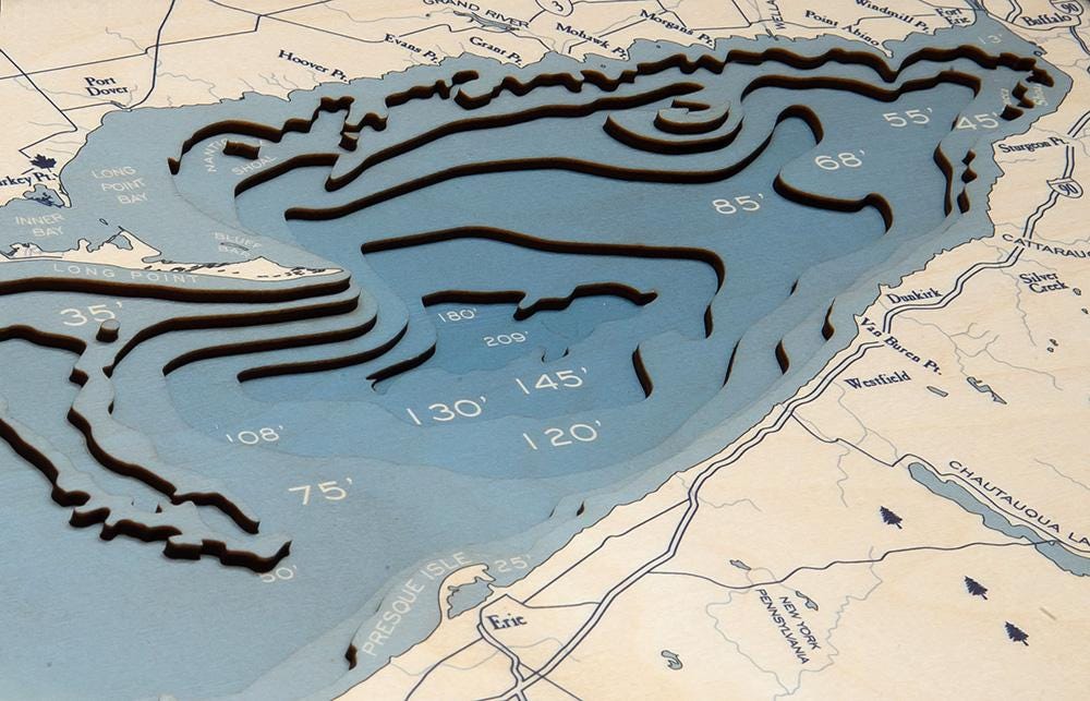 Lake Erie 3D layered wood map in laser-cut Baltic birch, shown framed against a light wall