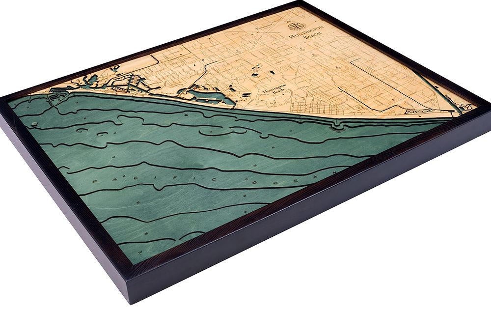 Huntington Beach, California 3D layered wood map in laser-cut Baltic birch, shown framed against a light wall