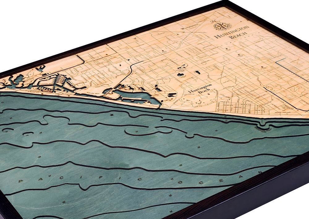 Huntington Beach, California 3D layered wood map in laser-cut Baltic birch, shown framed against a light wall