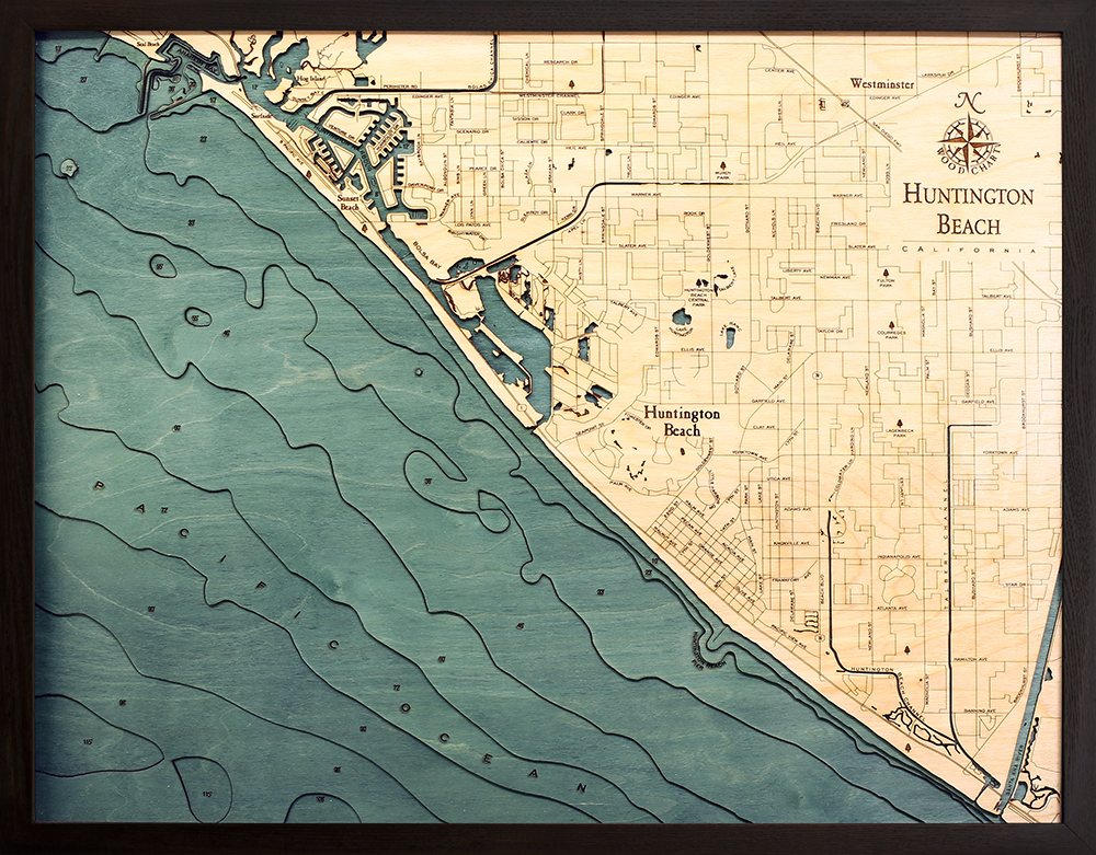 Huntington Beach, California 3D layered wood map in laser-cut Baltic birch, shown framed against a light wall