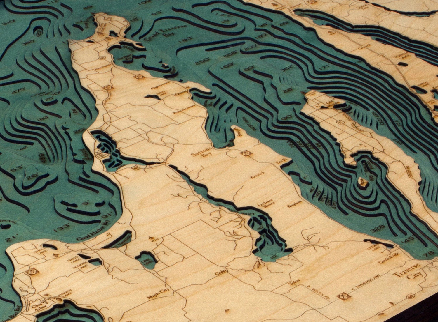 Grand Traverse Bay, Michigan 3D layered wood map in laser-cut Baltic birch, shown framed against a light wall