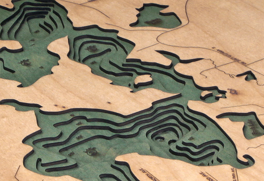 Arbutus (Traverse), Michigan 3D layered wood map in laser-cut Baltic birch, shown framed against a light wall