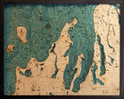 Grand Traverse Bay, Michigan 3D layered wood map in laser-cut Baltic birch, shown framed against a light wall
