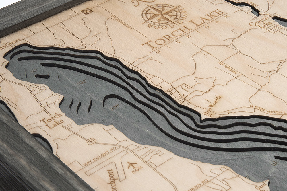 Torch Lake, Michigan 3D layered wood map in laser-cut Baltic birch, shown framed against a light wall