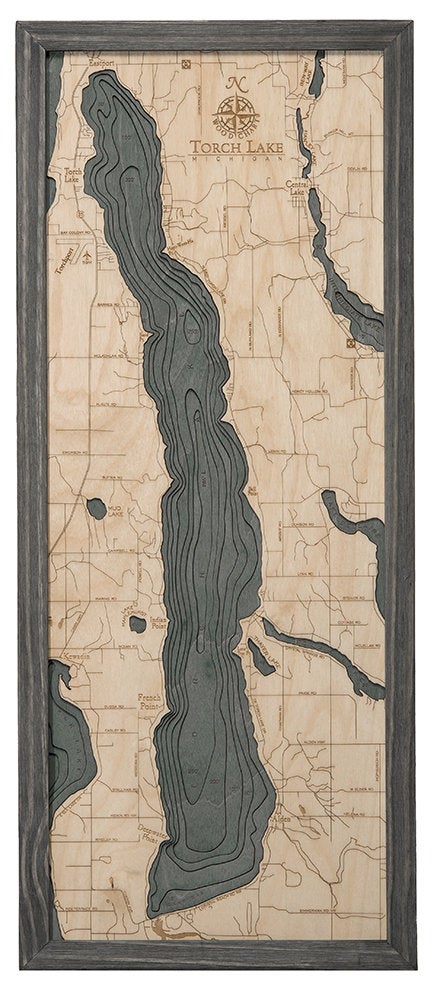 Torch Lake, Michigan 3D layered wood map in laser-cut Baltic birch, shown framed against a light wall