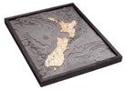 New Zealand 3D layered wood map in laser-cut Baltic birch, shown framed against a light wall