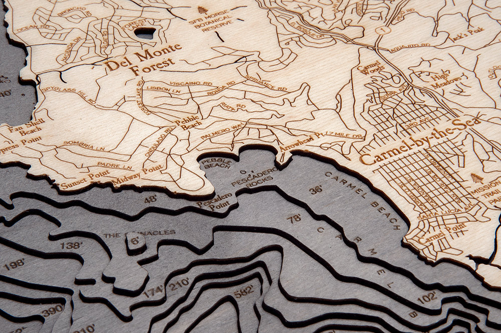 Carmel & Monterey, California 3D layered wood map in laser-cut Baltic birch, shown framed against a light wall