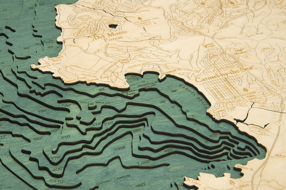 Carmel & Monterey, California 3D layered wood map in laser-cut Baltic birch, shown framed against a light wall